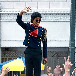 Sósia de Michael Jackson com uma jaqueta militar acenando para uma multidão.