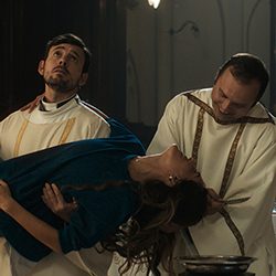 Dois padres carregando uma mulher de vestido azul prestes a desmaiar.