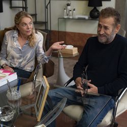 Mulher gesticula sentada à frente de um homem, em uma sala de escritório.