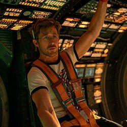 Ryan Gosling sentado, preso por cintos, dentro da cabine de comando complexa de uma espaçonave.