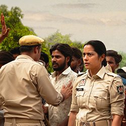 Shahana Goswami como uma policial com um olhar preocupado em meio a uma multidão.