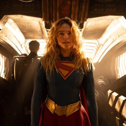 Supergirl com sua fantasia azul e vermelha dentro de uma nave espacial.