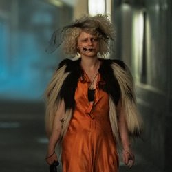 Mulher com cabelo loiro e um véu usando um vestido laranja e jaqueta de pele.