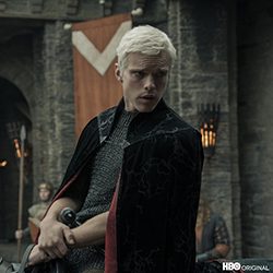 Homem loiro com armadura medieval e capa preta.