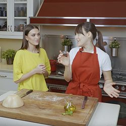 Duas mulheres em uma cozinha, uma usando um avental vermelho, preparando comida.