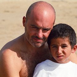 Homem careca sem camisa abraça um menino com camiseta branca.
