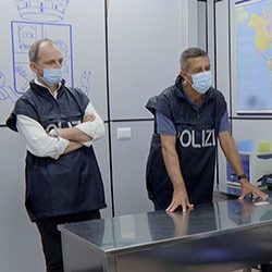 Dois policiais com uniformes azuis em um corredor bem iluminado.