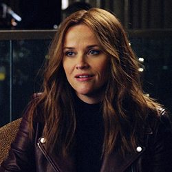 Close-up de uma mulher com cabelo castanho comprido sorrindo levemente.