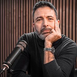 Homem descansa o queixo sobre a mão em frente a um microfone de podcast.
