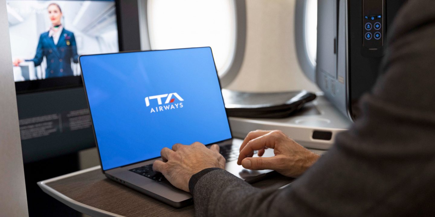 Gros plan d’une personne tapant sur un ordinateur portable, l’écran affichant le logo ITA Airways sur un fond bleu.