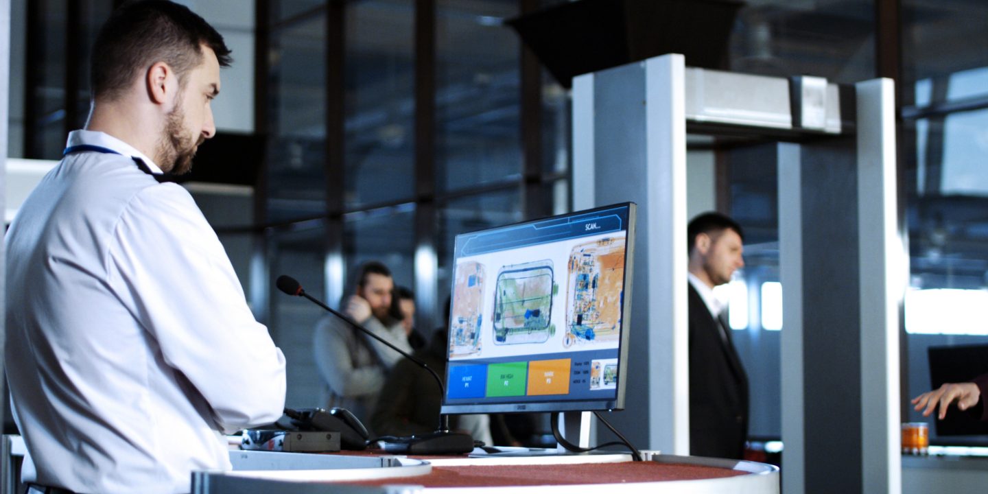 Airport employee monitoring screens at security checkpoints.