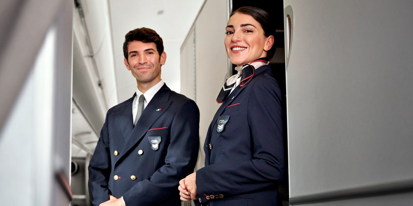 Two cabin crew members standing in the aisle of an aircraft.
