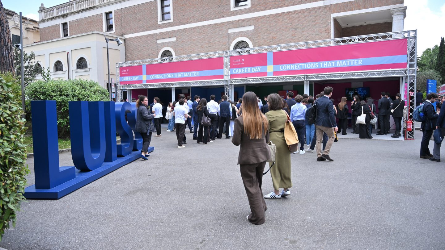Studenten buiten bij een groot blauw LUISS-teken.