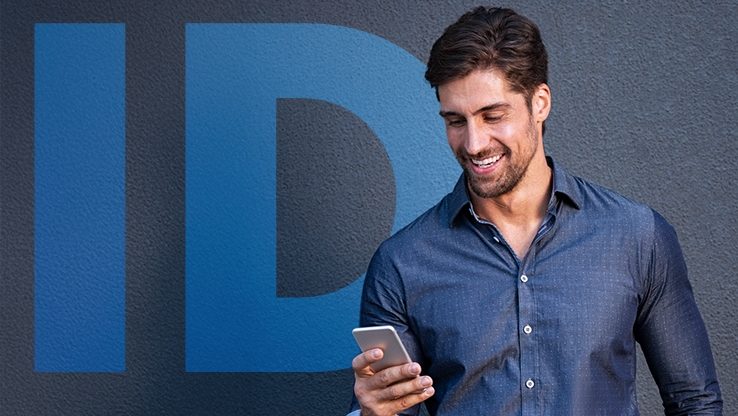 Ένας άνδρας κοιτάζει ένα smartphone ενώ στέκεται μπροστά σε έναν τοίχο με την ένδειξη «ID».