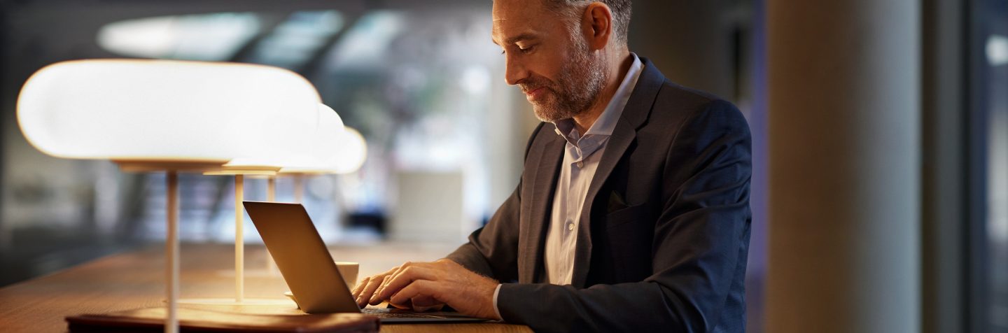 Businessman typing on a laptop at a warmly lit modern desk.