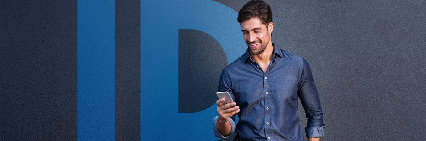 A man looking at a smartphone while standing in front of a wall with the word “ID” displayed.