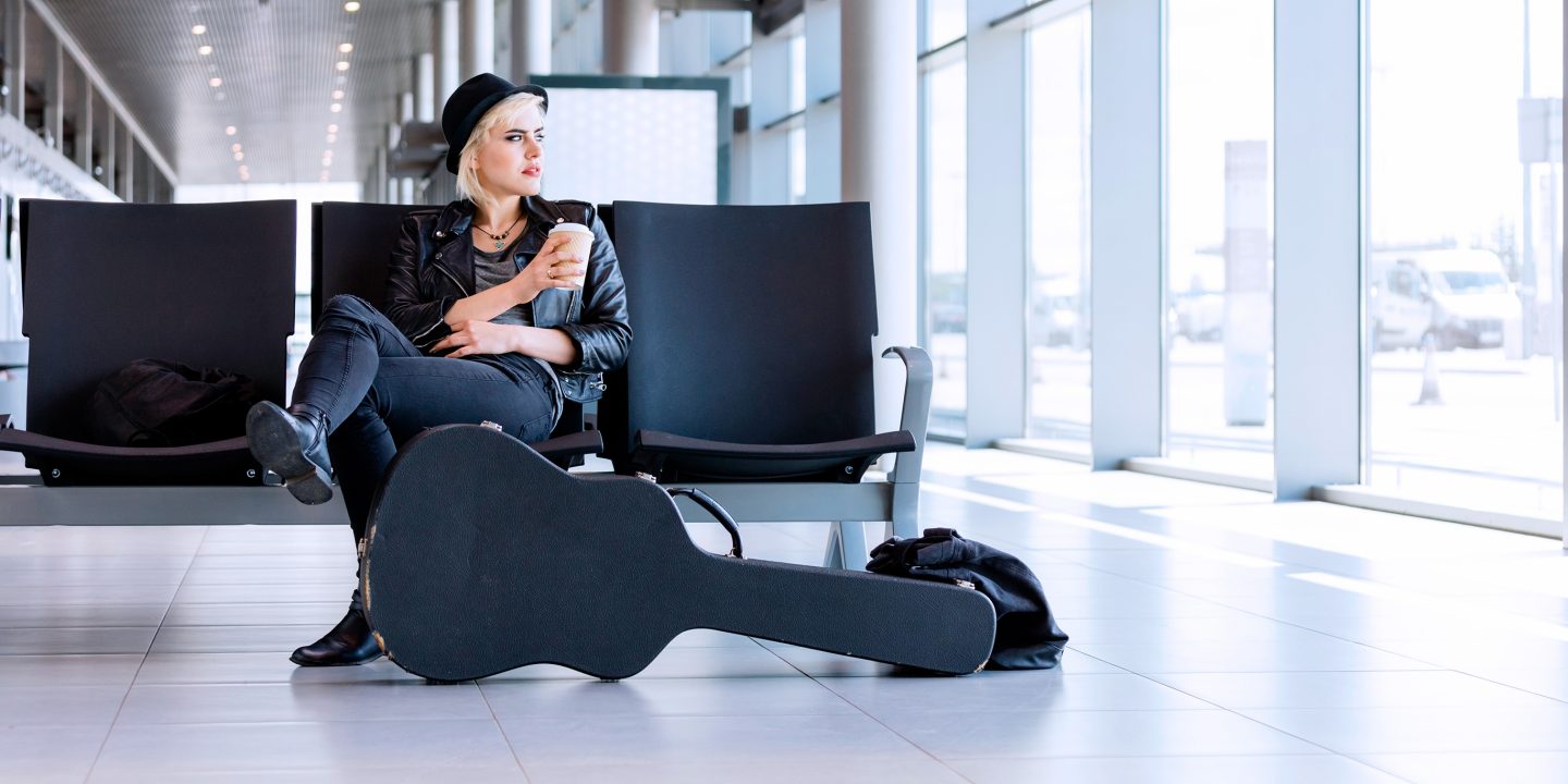 Eine Frau sitzt auf einer Sitzreihe im Flughafen und hält einen Becher Kaffee zum Mitnehmen in der Hand.