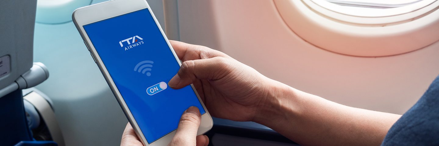 Une main tient un smartphone affichant le logo d’ITA Airways et le symbole Wi-Fi à bord de l’avion.
