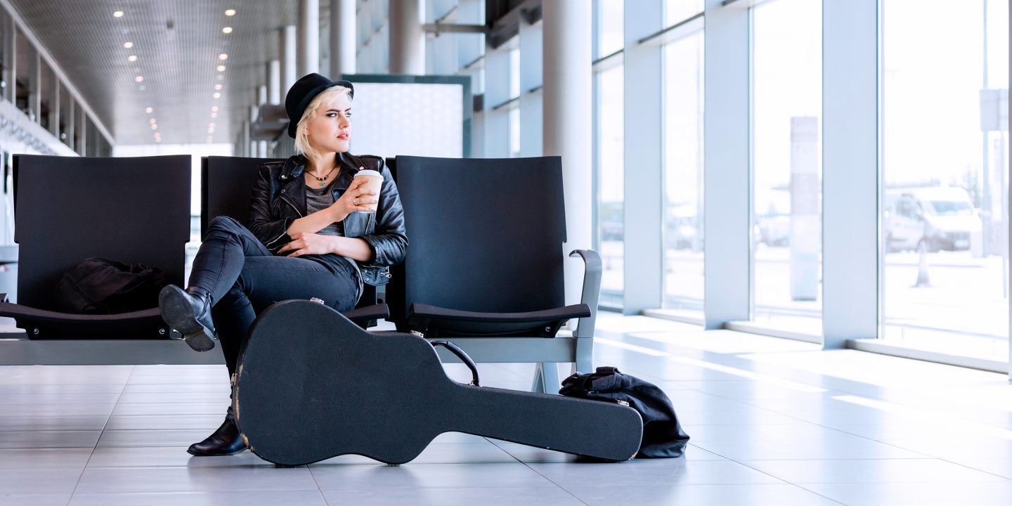 Eine Frau sitzt auf einer Reihe von Sitzen im Flughafen und hält einen Becher Kaffee zum Mitnehmen in der Hand.