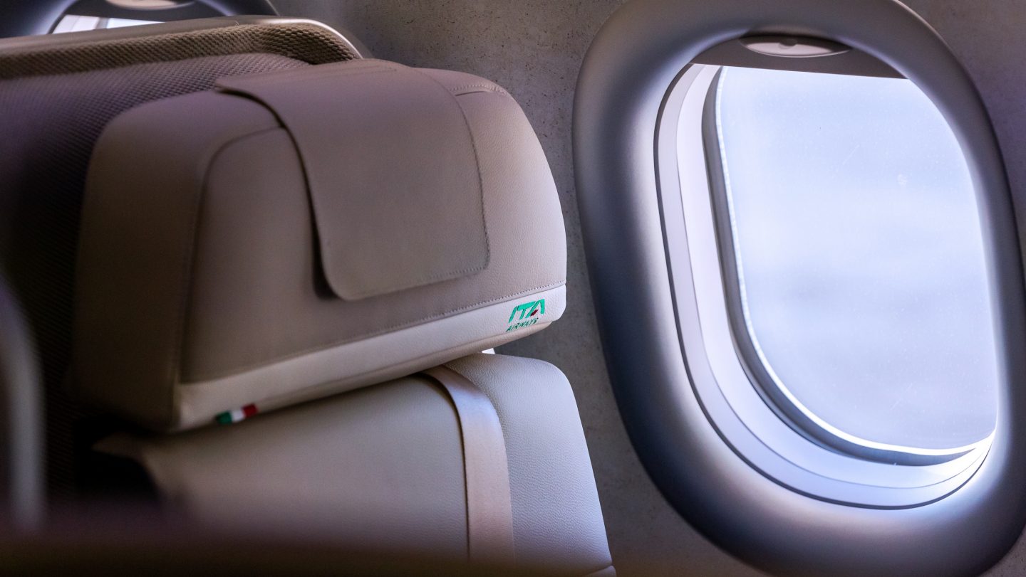 機窓を前景に捉えた、ビジネスクラス座席ヘッドレストのクローズアップ。