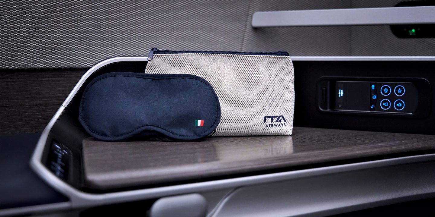 Oogmasker van ITA met een geborduurde Italiaanse vlag en een toilettas met ITA-logo op de tafel.