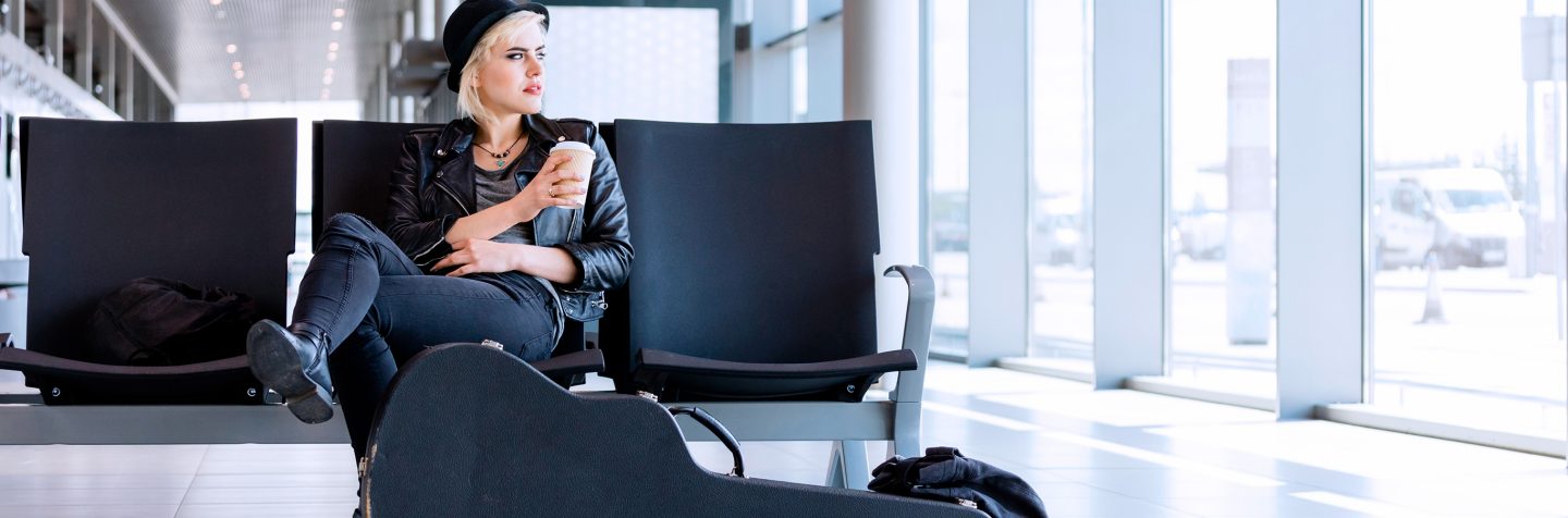 Een vrouw zit op een rij stoelen op de luchthaven met een beker afhaalkoffie in haar hand.