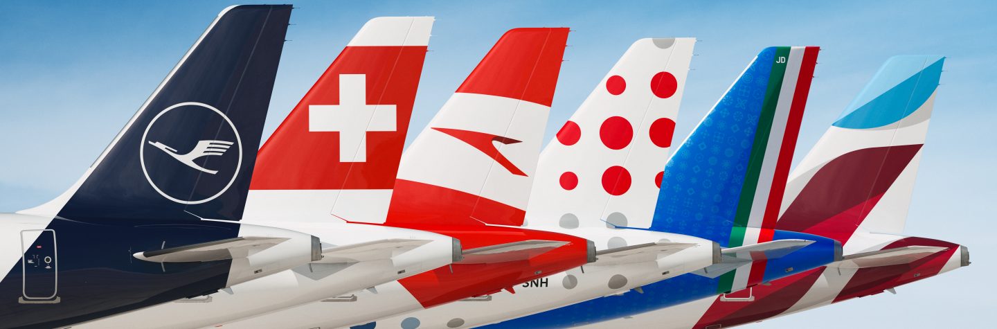 Aletas traseiras de aeronaves Lufthansa, SWISS, Austrian Airlines, Brussels Airlines, ITA Airways e Eurowings alinhadas em frente a um céu azul.